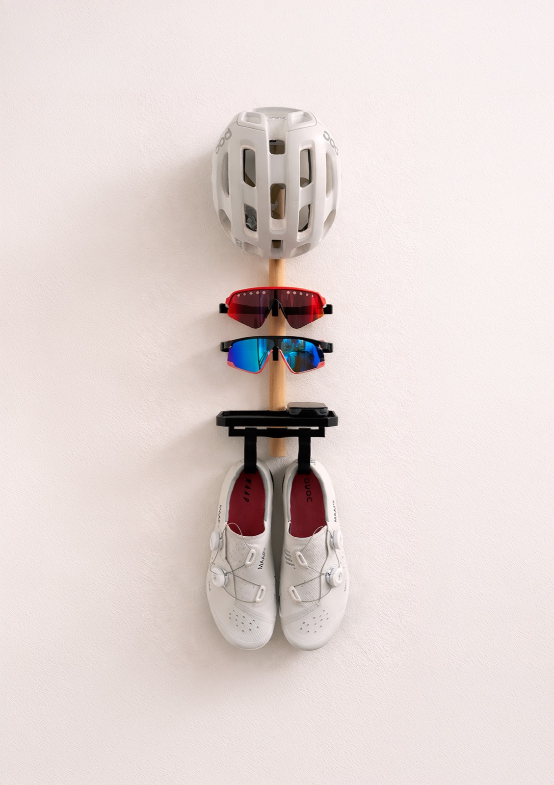 Wall-mounted Faster Stands cycling organizer holding a helmet, two pairs of glasses, and cycling shoes.